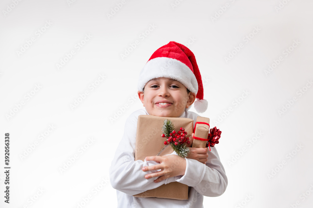A boy in a red Santa hat smiles and hugs boxes of gifts. Christmas concept. A boy in a red Santa hat smiles and hugs boxes of gifts. Christmas concept.