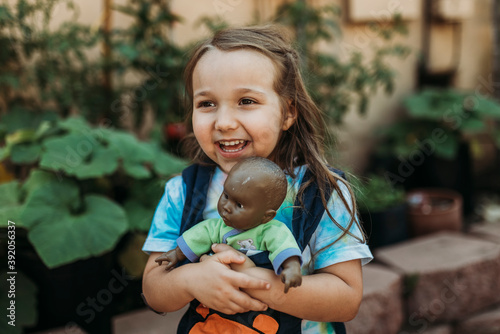 Preschool aged girl carrying babydoll in baby carrier in garden photo