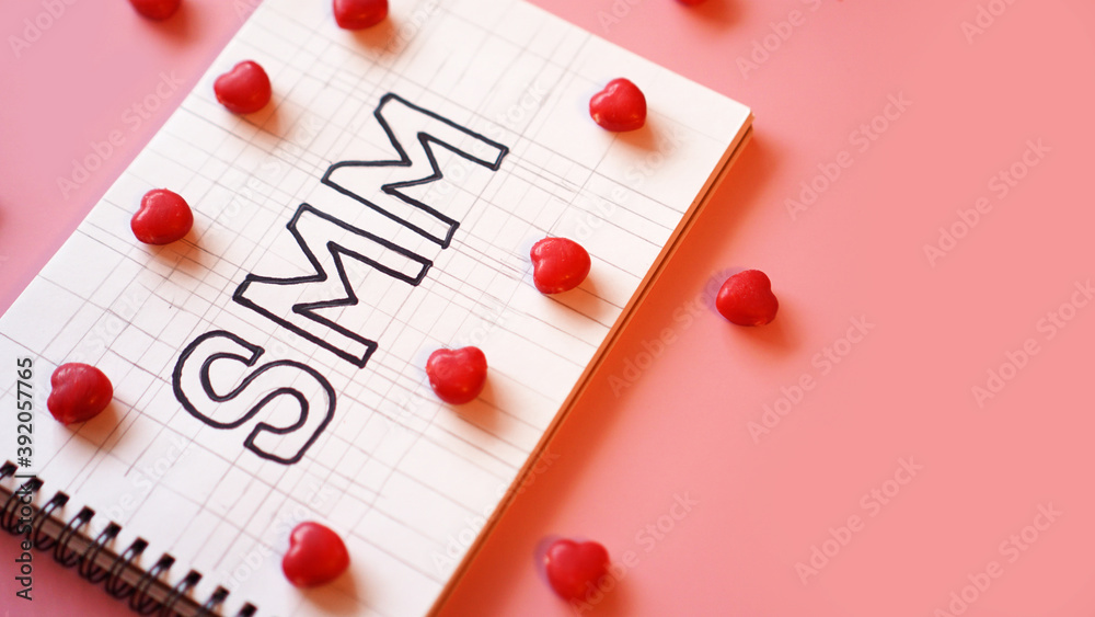 SMM Social media marketing text on on notebook on pink background with candy in the form of hearts SMM Social media marketing text on on notebook on pink background with candy in the form of hearts