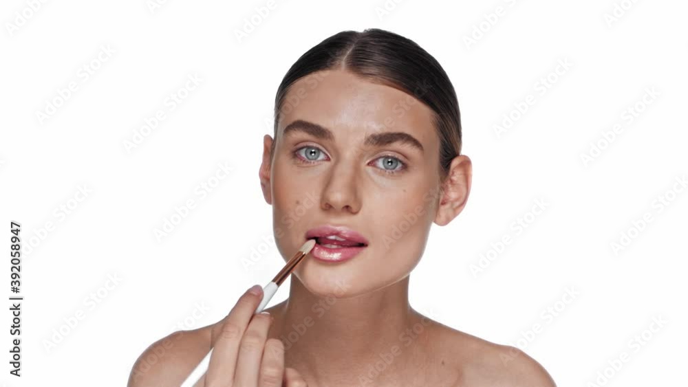 Young adult woman applying lip gloss with cosmetic brush isolated on white