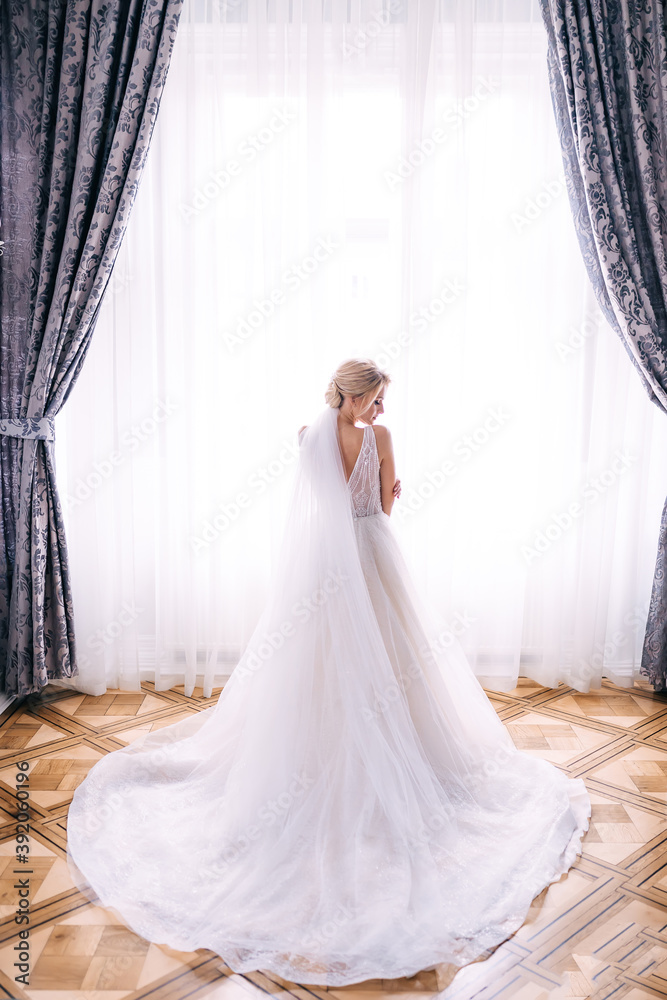 the bride in a luxurious white dress stands near the window the bride in a luxurious white dress stands near the window