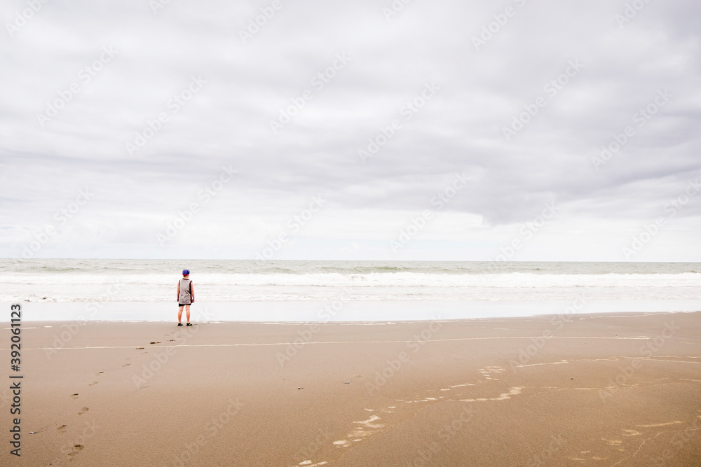 Young boy standing on the beach looking at the water Young boy standing on the beach looking at the water
