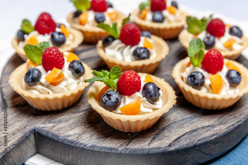 Fruit and berry tartlets dessert assorted on wooden tray. Closeup of delicious pastry sweets pies colorful cakes with fresh natural raspberry blueberry and cheese cream. French bakery catering.