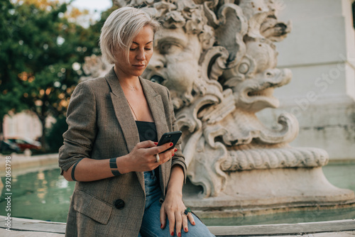 Woman texting in her mobile phone while sitting at fountain photo