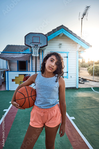 A girl with curly hair standing on the basketball court of her own home