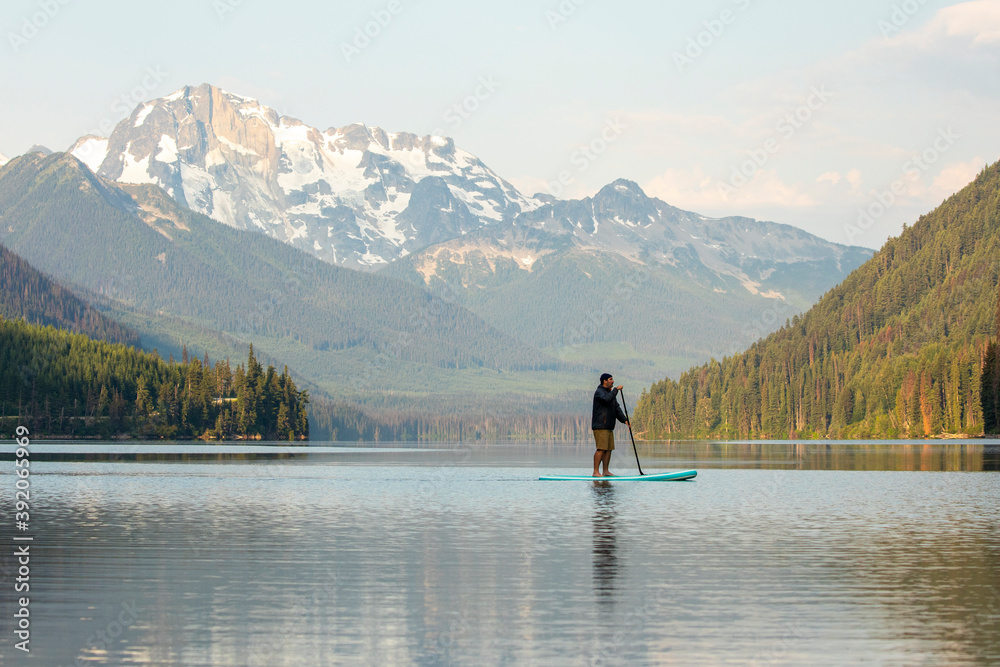 Side view of male on paddle board Duffey Lake on background of spectacular mountain ridge in morning in British Columbia Side view of male on paddle board Duffey Lake on background of spectacular mountain ridge in morning in British Columbia