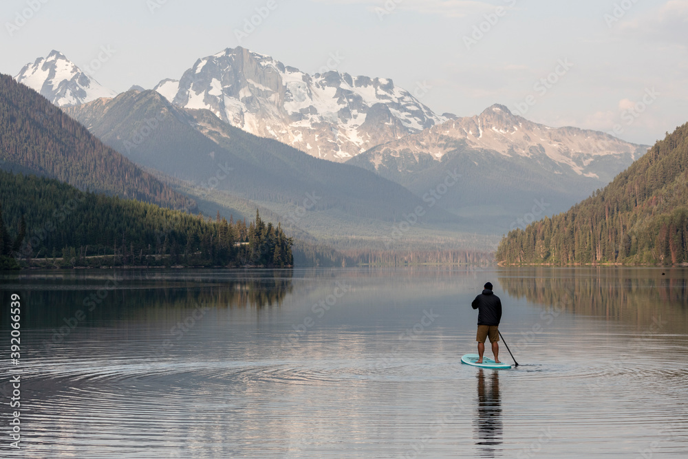 Back view of anonymous male on paddleboard on calm surface of Duffey lake and enjoying landscape of mountains in morning in British Columbia Back view of anonymous male on paddleboard on calm surface of Duffey lake and enjoying landscape of mountains in morning in British Columbia