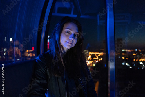 Young happy woman sitting in ferris wheel booth riding on attraction, blue light