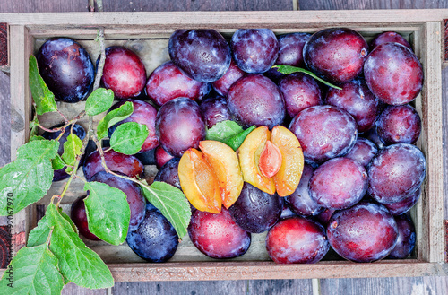 fresh blue plums with leaves in wooden box, top view