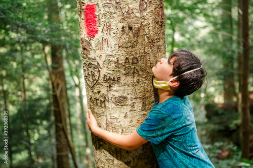 A small boy sadly hugs a tree trunk scarred with graffiti photo