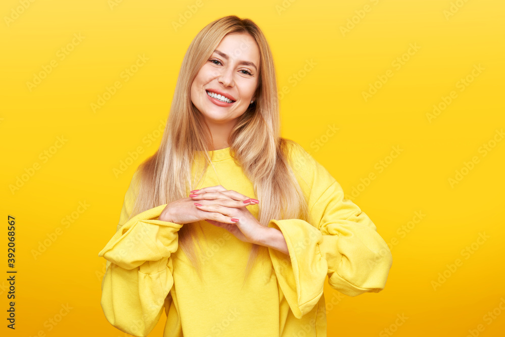 Portrait of pleasant looking glad happy young blonde woman smiling, posing and looking at the camera isolated in yellow studio. Enjoy life concept Portrait of pleasant looking glad happy young blonde woman smiling, posing and looking at the camera isolated in yellow studio. Enjoy life concept