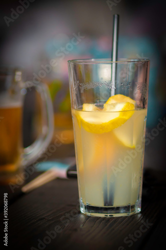 bright lucent yellow drink (lemonade) with lemon slices and in dark close up, on a wood table, non-alcoholic drink