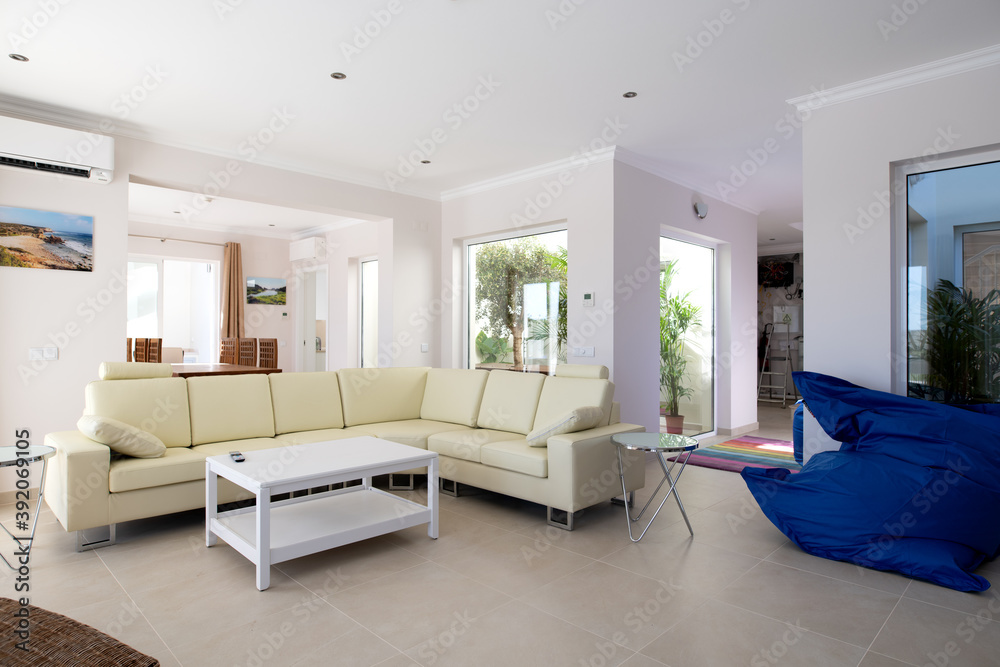 Fototapeta premium Modern, clean living room of luxury family house with large l-shape leather sofa and tiled floors