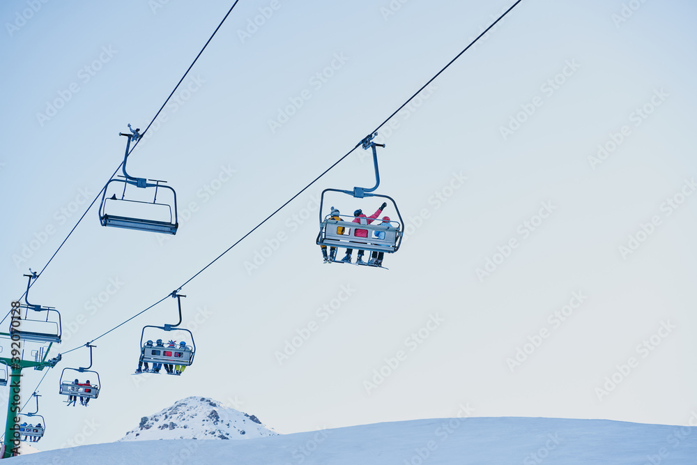 Skiers on a chairlift looking down with a blue background Skiers on a chairlift looking down with a blue background