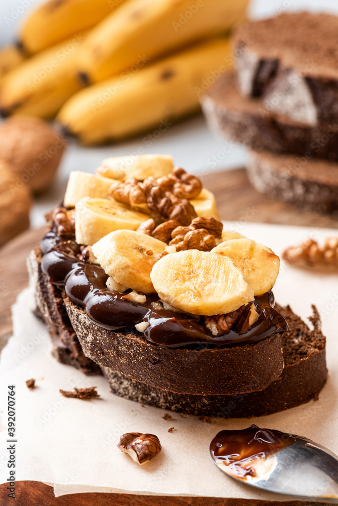 Toast with rye bread, chocolate, bananas, and walnuts on a wooden table. Close-up, selective focus.