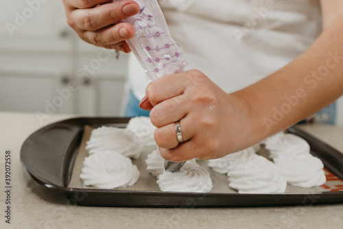 А photo of the hands of a woman who is putting the freshly whipped meringue on a tray with a pastry bag with an asterisk attachment. A girl is preparing to cook a delicious lemon meringue tart.