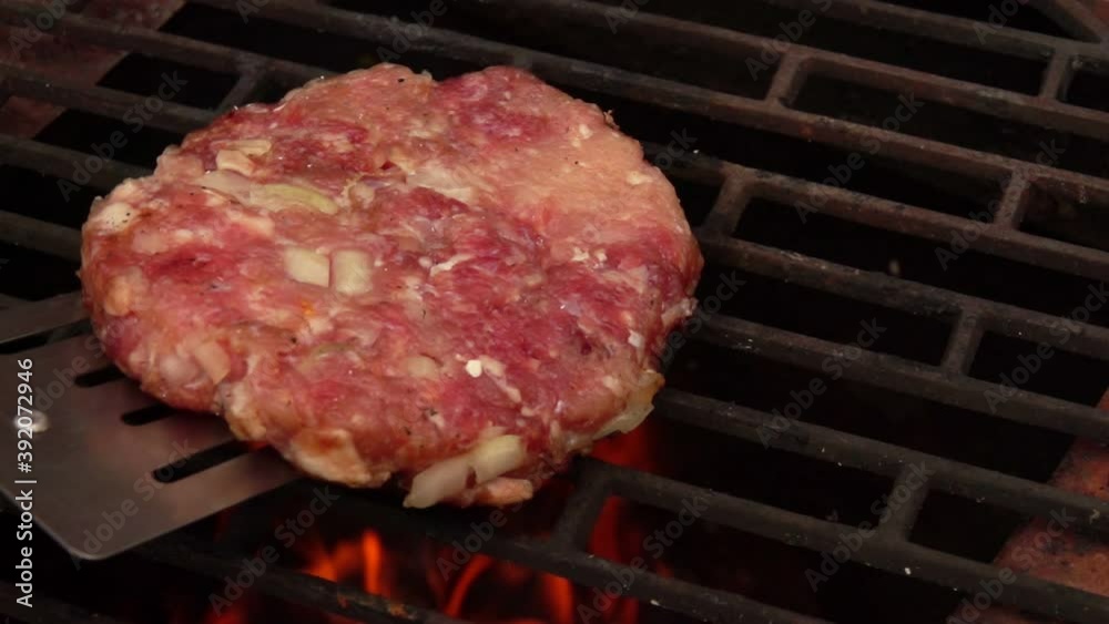 Raw homemade cutlet for a burger is placed on the grill grid above the open fire outdoors Raw homemade cutlet for a burger is placed on the grill grid above the open fire outdoors