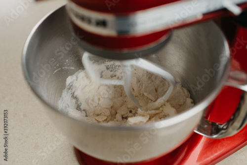 A close photo of a red stand mixer which is whipping butter, almond flour, and wheat flour fast to the shortcrust pastry in a stainless steel mixing bowl in a kitchen.