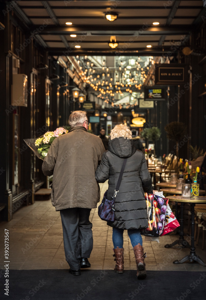Adult couple in love. A couple walking through a shopping area, the man carries a bouquet of flowers and the woman some bags with gifts