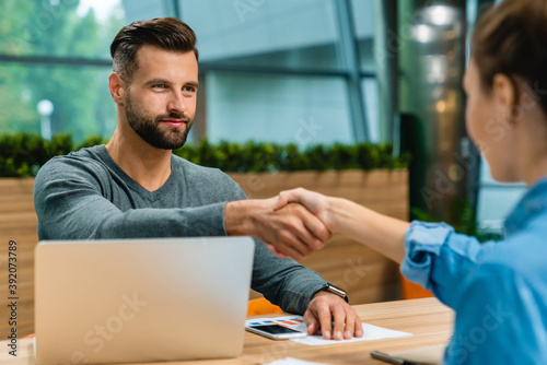 Two young business partners shaking hands at office desk