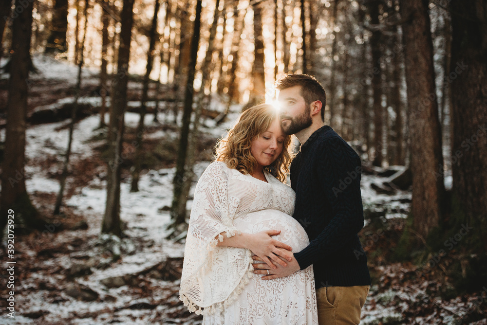 Husband and pregnant wife in the forest on a snowy sunny winter day Husband and pregnant wife in the forest on a snowy sunny winter day