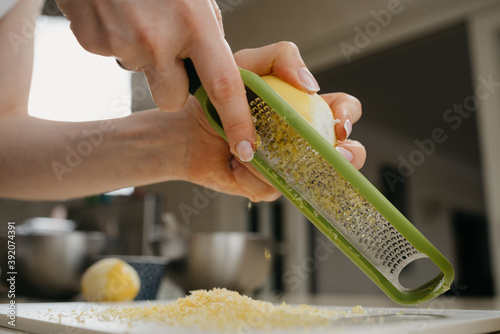 A close dynamic photo from below of the hands of a woman who is separating the lemon zest with a grater in the kitchen photo