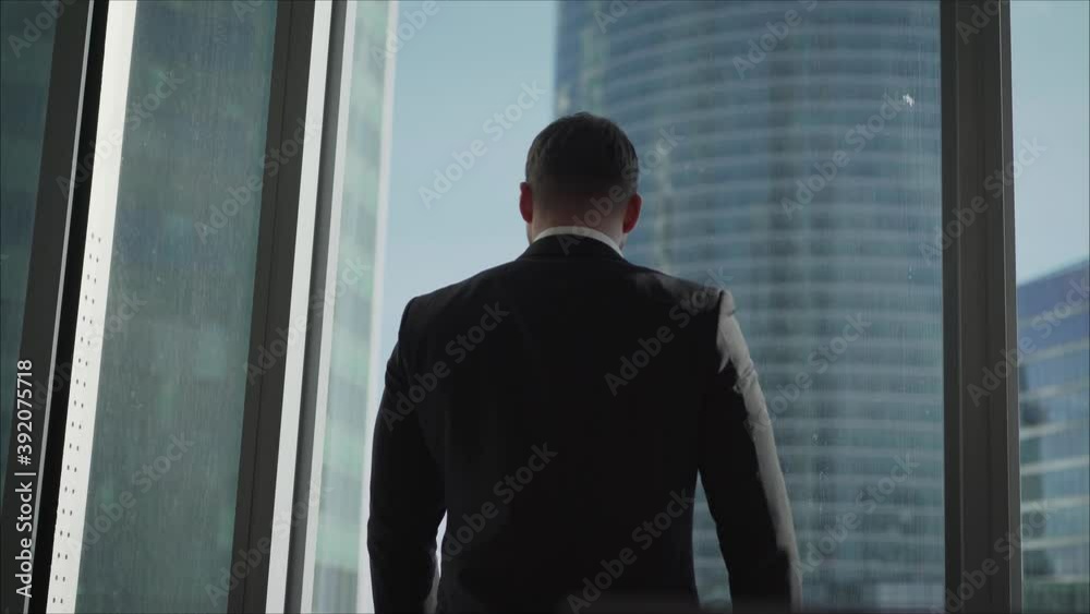 A successful businessman stands at a panaram window against the backdrop of skyscrapers. Mature successful businessman in a modern office building. A successful handsome businessman in a suit stands A successful businessman stands at a panaram window against the backdrop of skyscrapers. Mature successful businessman in a modern office building. A successful handsome businessman in a suit stands