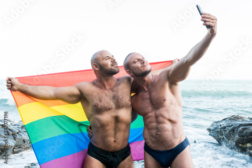 Lgbt pride concept. Gay bear couple holding rainbow flag with open arms taking a selfie photo. photo