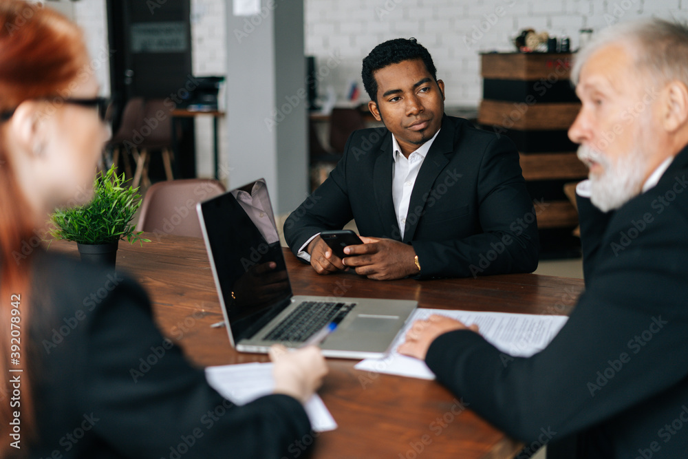 Skilled mature adult male businessman having meeting with young diverse multi-ethnic business colleagues in modern office. Multiethnic business team of businessmen people discussing new project.