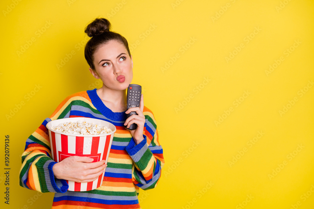 Photo of young attractive woman think hold remote control eat pop-corn look empty space isolated over yellow color background - obrazy, fototapety, plakaty 