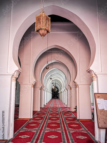 The interior Islamic beauty of the Koutoubia mosque in Marrakesh. The mosque has red Moroccan carpets laid down on the ground with white arches and a long hallway