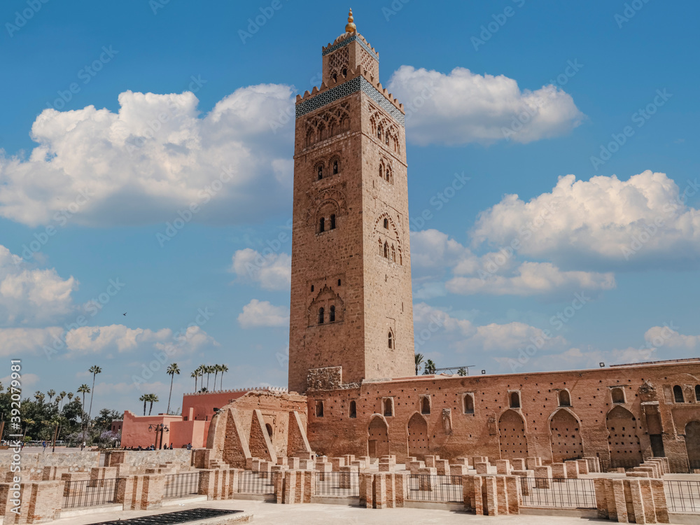 view of the famous tower Kutubiyya Mosque in Marrakesh with its temple in the foreground. Very cloudy summer sky in the background