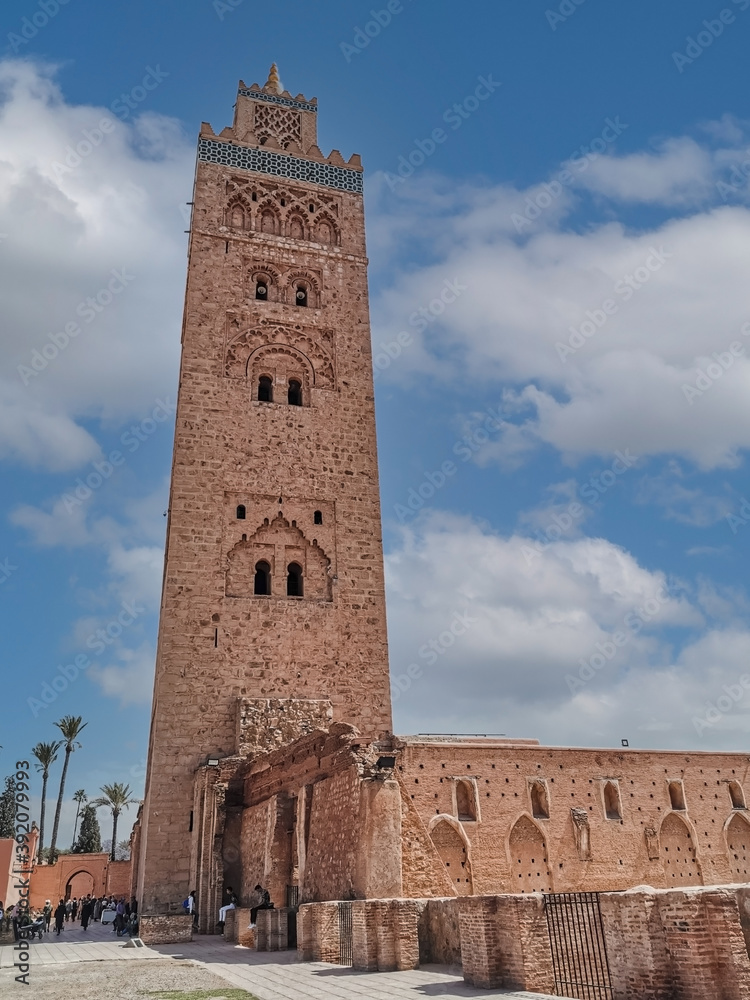 view of the famous tower Kutubiyya Mosque in Marrakesh with a clear sky and people sitting next to the building