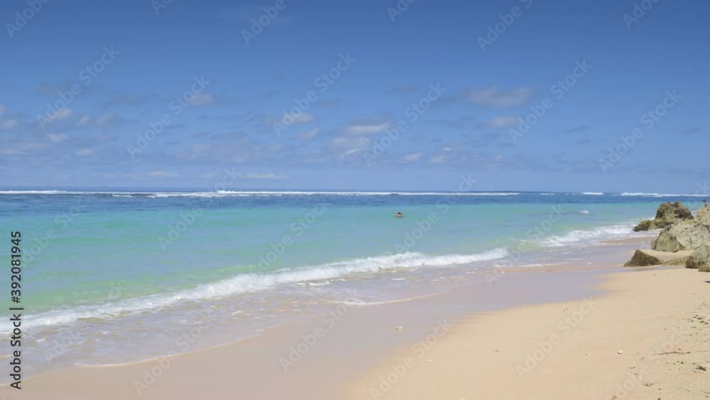 Tropical beach with big waves near reef and beautiful vibrant water is splashing yellow sand and people are swimming in ocean Tropical beach with big waves near reef and beautiful vibrant water is splashing yellow sand and people are swimming in ocean