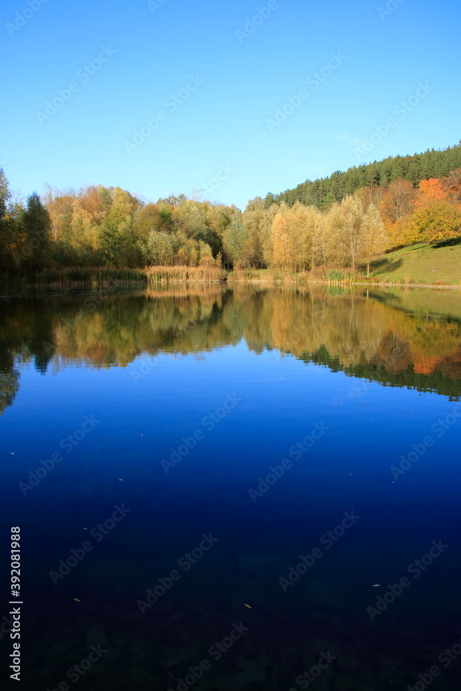 Blick auf den Gültlinger See. Der Herbstwald spiegelt sich im See.