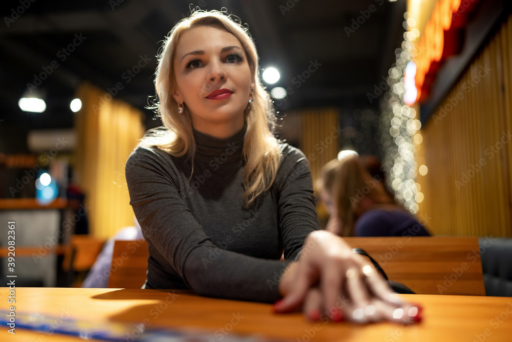 Fototapeta premium Portrait of a young blonde girl in a cafe in the evening.