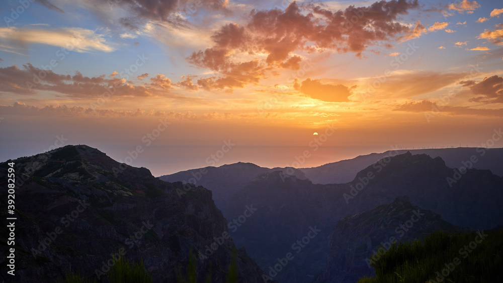 Postcard from Madeira. Sunset over mountains from the highest point of mountain Pico do Arieiro. Twilight, sun touches ocean. Tranquil moment. Traveling around Madeira Island, Portugal.