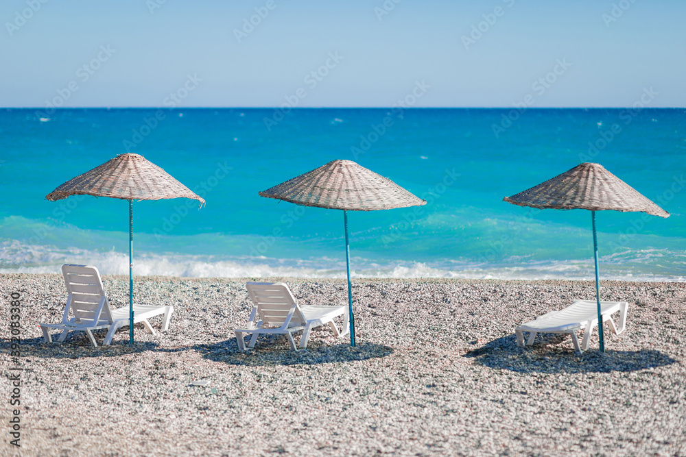 Very beautiful view of the beach with pebbles and the blue ocean or the azure sea with white sun loungers and wicker umbrellas. The concept of a postcard about a vacation, rest in paradise, travel.
