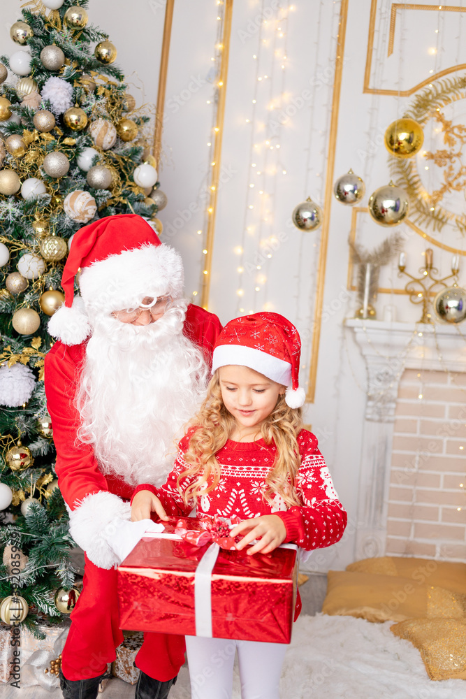 Santa Claus gives a baby girl a gift at the Christmas tree, the concept of new year and Christmas