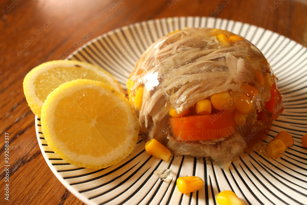 Poultry jelly (galantine) with corn and carrots, served with lemon slices on a black and white plate Poultry jelly (galantine) with corn and carrots, served with lemon slices on a black and white plate