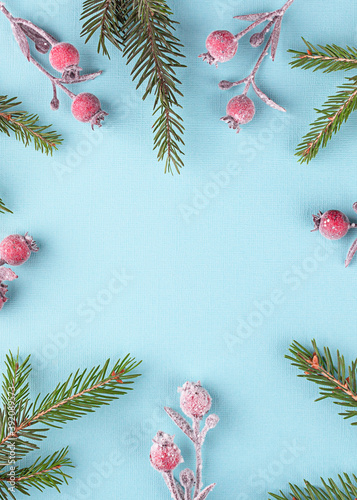 Creative Christmas template with copy space in the center. Branches of spruce and red berries on a light blue background. Flat lay. 