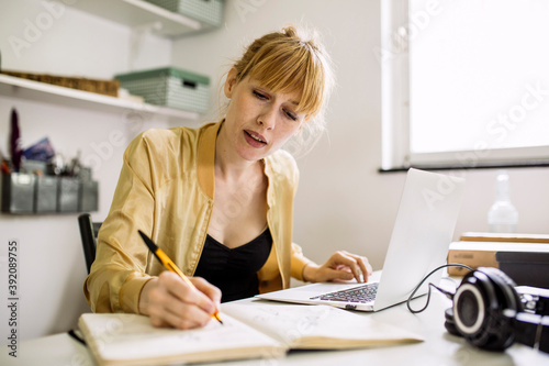 Woman working from home taking notes in note book