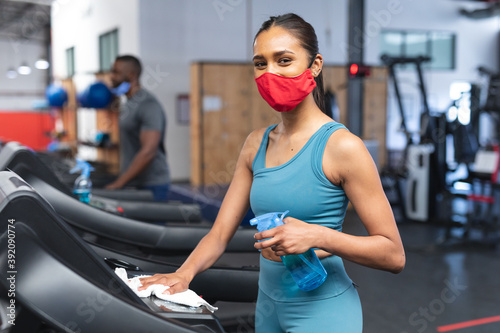 Portrait of fit caucasian woman wearing face mask sanitizing cardio machine before working out in th