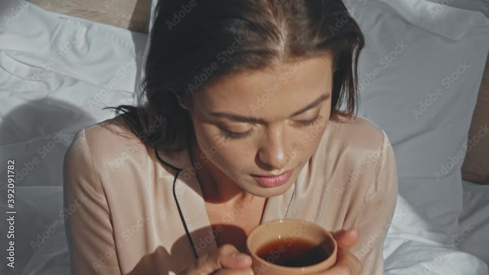 joyful woman drinking tea while sitting in bed
