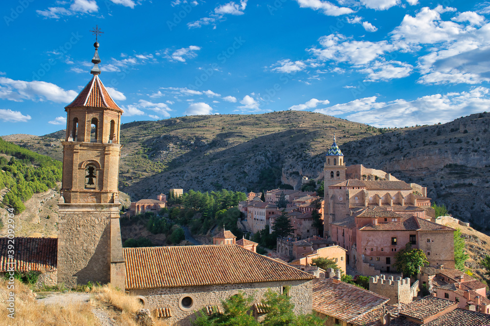 Leaning bell tower of the Santa Maria y Santiago parish in the beautiful medieval town of Albarracin, Teruel. Salvador Cathedral in the background on a hill, Spain