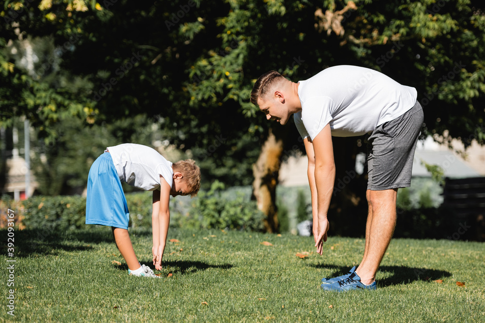 Man and boy in sportswear with outstretched hands, leaning forward in park with blurred trees on background Man and boy in sportswear with outstretched hands, leaning forward in park with blurred trees on background