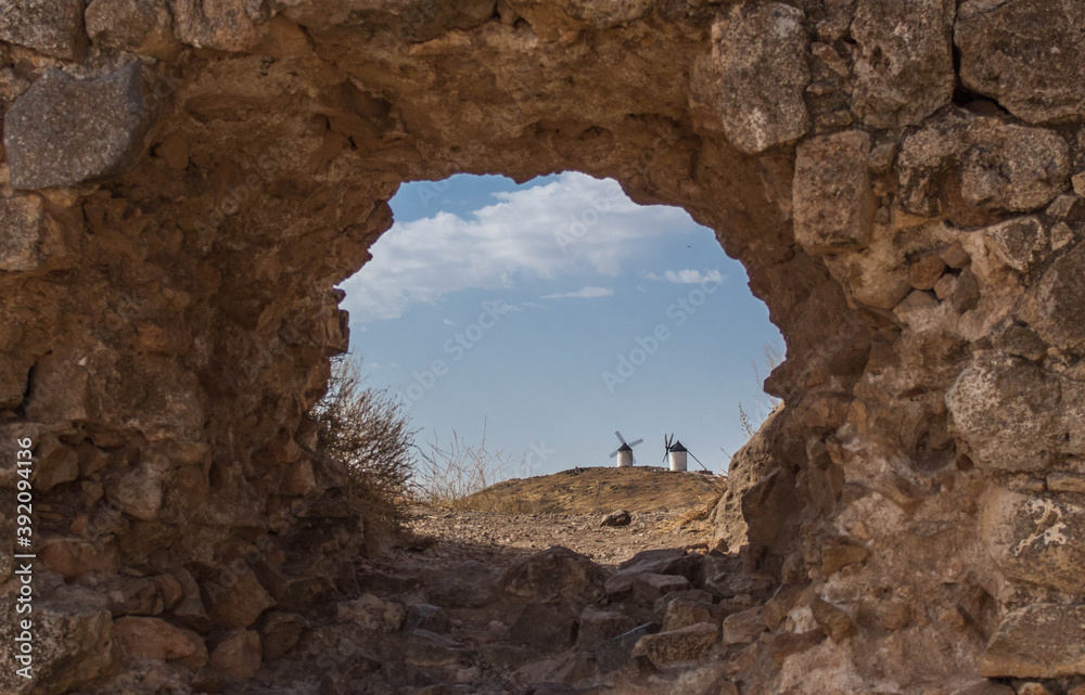 Molinos de viento vistos a través de un agujero hecho en un muro de piedra.
