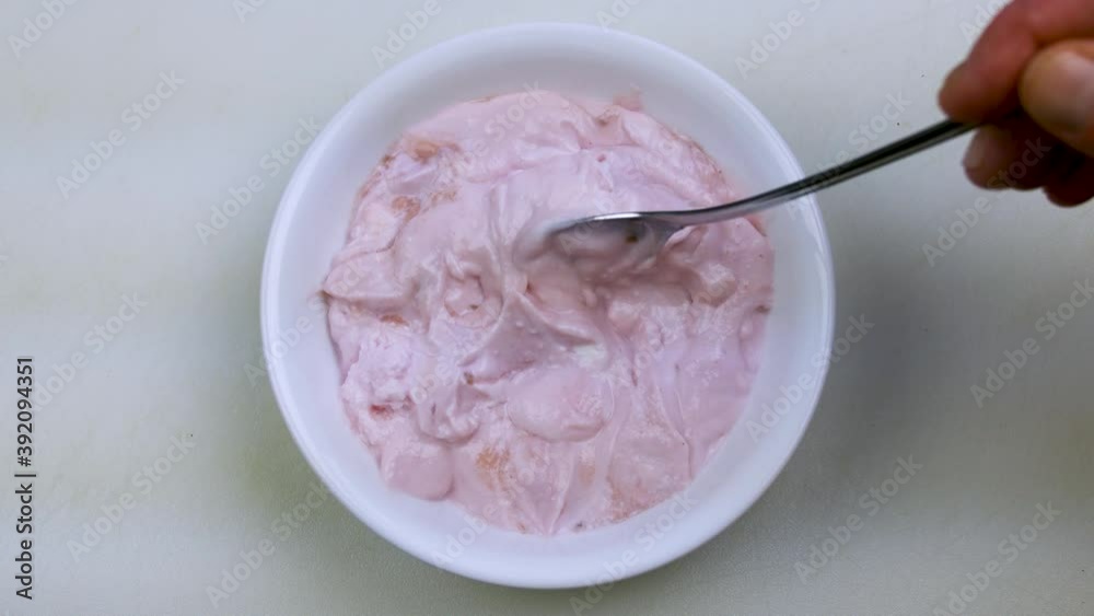 Video of stirring raspberry Greek yogurt in a white bowl that moves around a lot with a spoon on a countertop. Video of stirring raspberry Greek yogurt in a white bowl that moves around a lot with a spoon on a countertop.