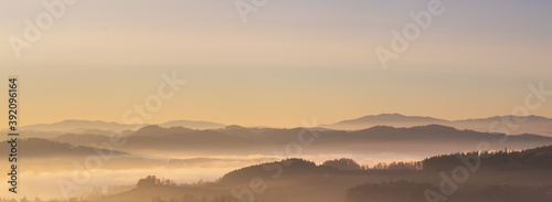 misty landscape at sunset, mountains rising from clouds of fog in the background, clear sky