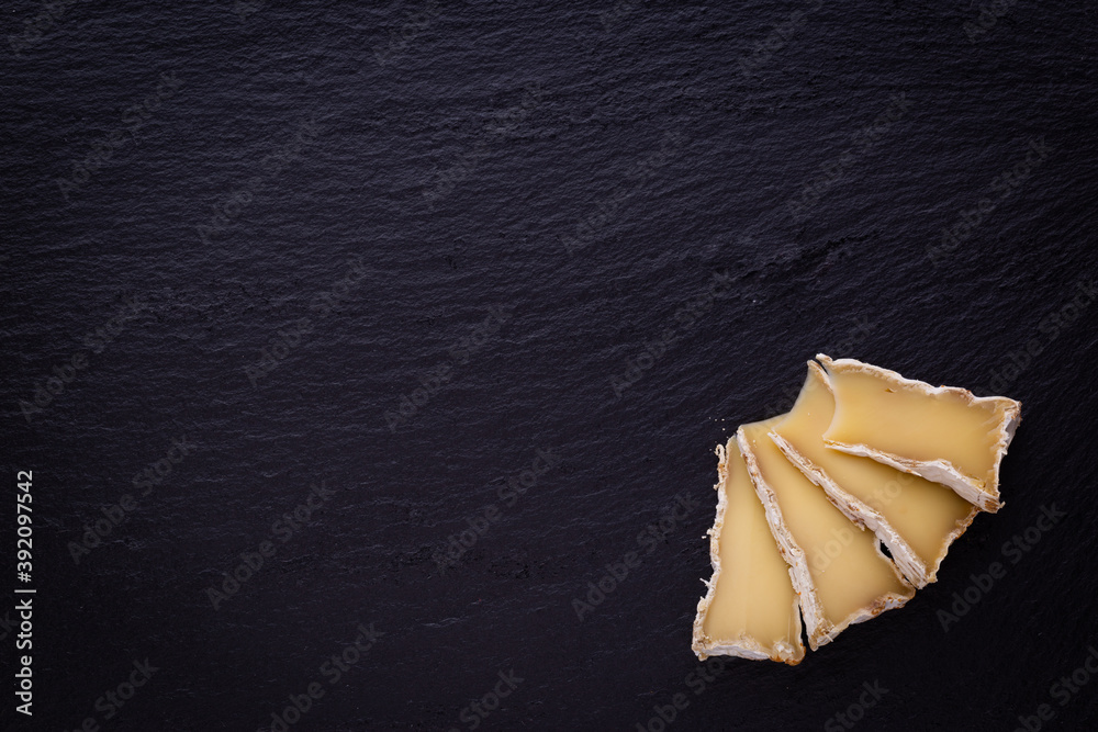 Aged brie cheese placed on black stone background with space for copy